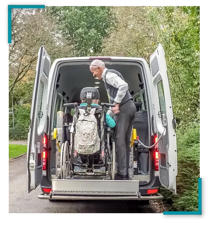 Oudere chauffeur assisteert dame in rolstoel met uitstappen aan de achterzijde van een aangepaste auto.